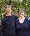 Portrait of researchers Asger Hobolth and Victoria Birkedal standing outdoors in front of green foliage, smiling at the camera. They co-lead a VILLUM Synergy project at Aarhus University.